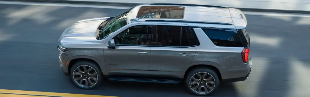 The image shows a silver Chevrolet Tahoe SUV driving on a city street.